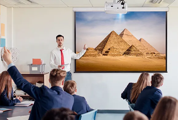 a professor in front of a classroom pointing at a projected image of the pyramids of giza