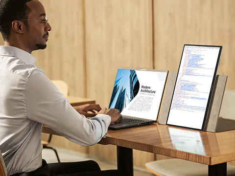 Man working at desk with laptop and portable monitor in portrait mode