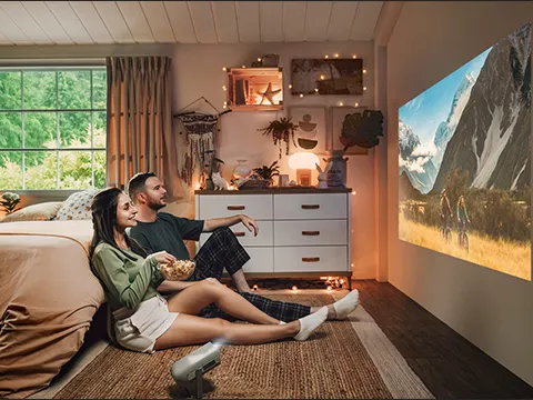 two people sitting on the floor in a bedroom watching a portable projector