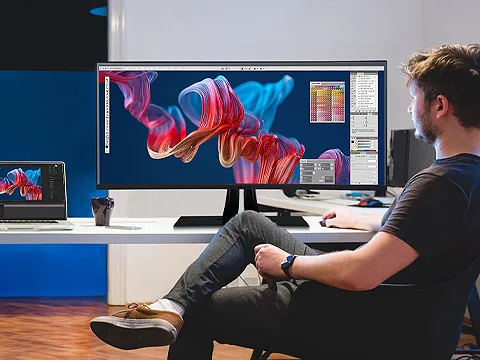 a man sits at a large monitor connected to a laptop
