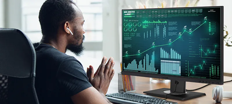 a man sitting at a desk looking at graphs on a monitor