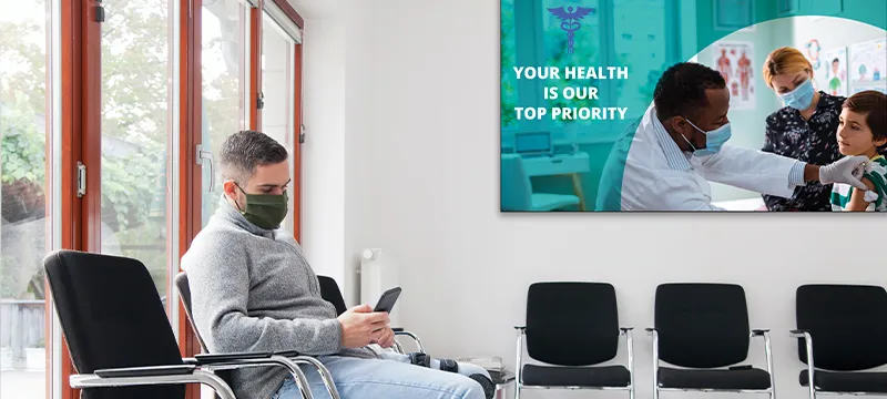 a man sitting in a waiting room wearing a mask while on his phone.