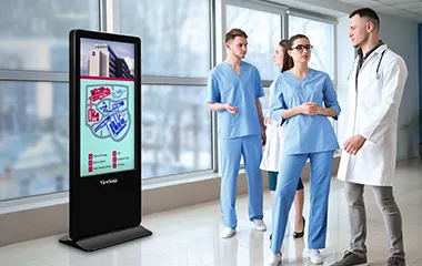 two nurses and a doctor stand next to a kiosk in a hallway