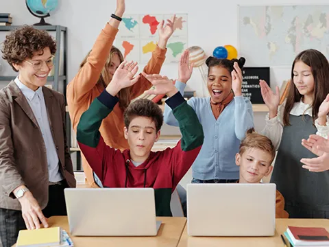 a group of students surround two on laptops as they all cheer