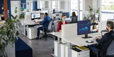 Employees sitting at their desks, working on their computers in a large office setting.