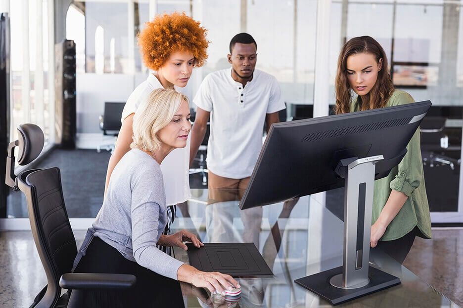a group of people surrounding a computer monitor in an office setting