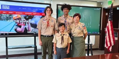 Three Boy Scouts and Scout Mom standing in a room, in front of two ViewBoards.