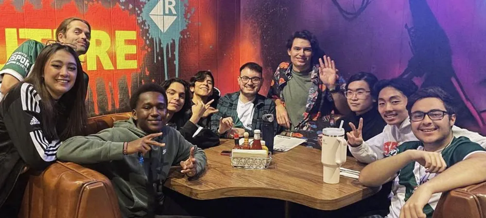 a group of teenagers and young adults crowded around a table in a corner booth