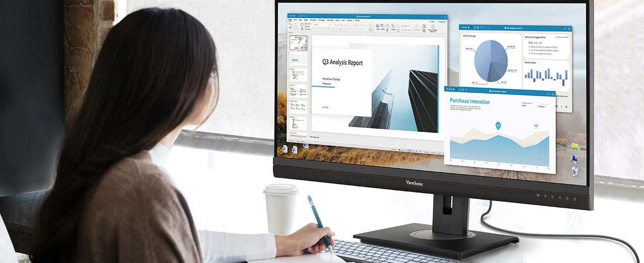 a woman using an ultrawide monitor with multiple windows open while taking notes in a notebook