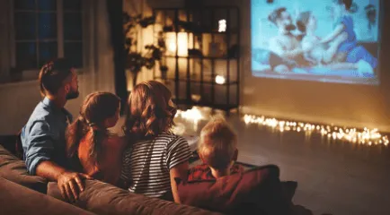 Family of four sitting on a couch in a dark room using a ViewSonic projector to watch a movie.